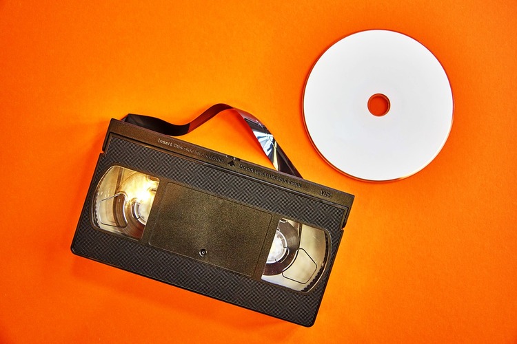 Een videocassette en een cd op een oranje achtergrond.